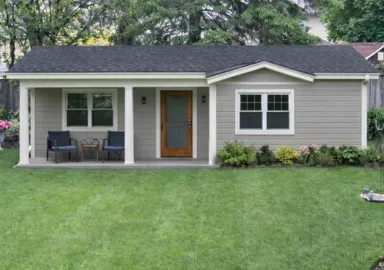 Small gray siding accessory dwelling unit with white columns, wooden door, and professional landscaping in Dallas, Texas.